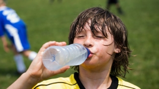 年轻男孩饮用水在踢足球以后
